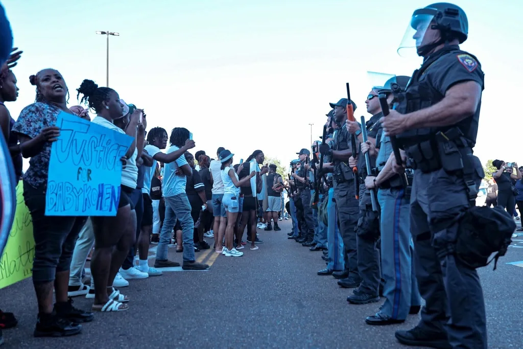 Community members calling for justice across from a line of police officers